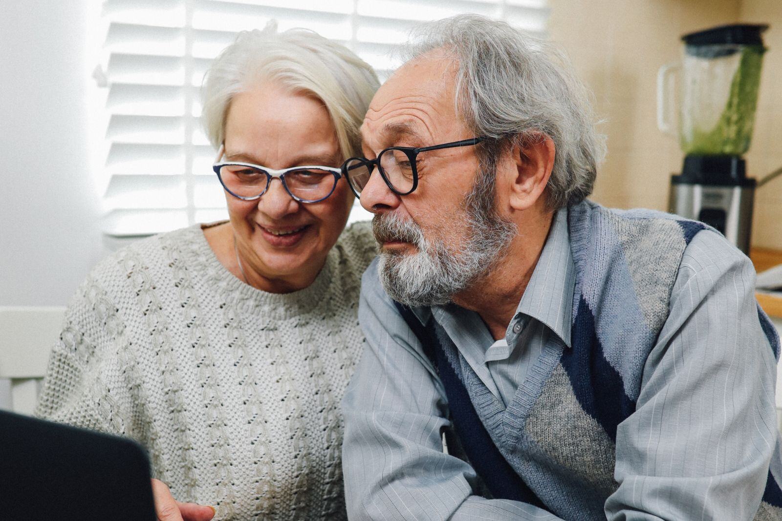 An older adult couple look together at a screen, researching their options.